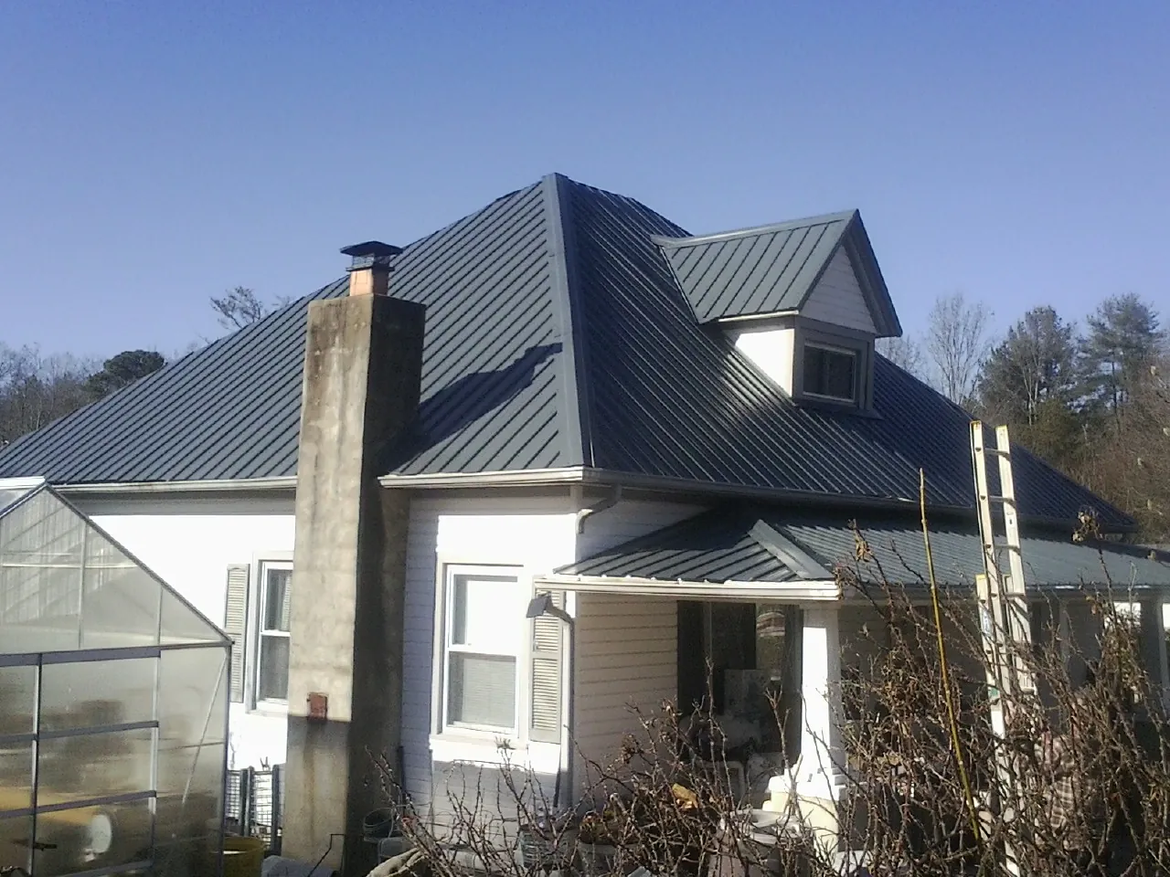 Dark blue standing seam metal roof on a white farmhouse with dormer — Slate & Tile Roof Repair by Roofing Brothers in Rio Medina