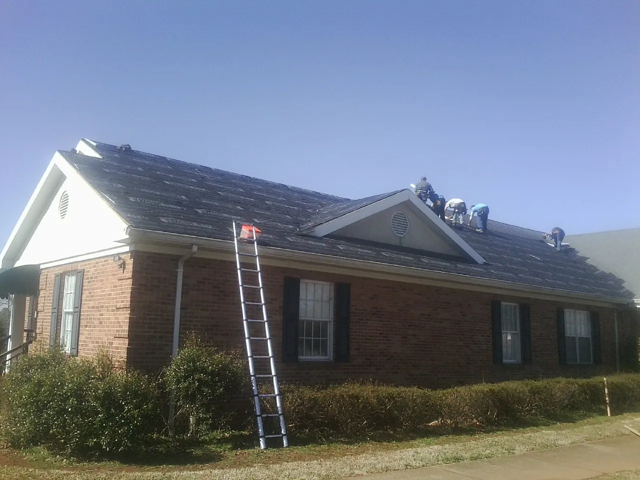 Crew tearing shingles off a brick ranch roof with a ladder set — Metal Roof Repair work by our crew in Rio Medina