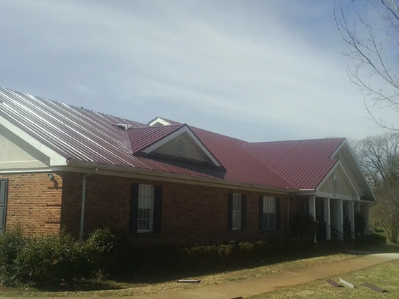 Red metal roof with gabled entries on a long brick building, from a Hail Damage Roof Repair job in Rio Medina