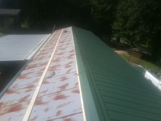 Old rusted panels beside newly installed green metal roofing — Wind Damage Roof Repair by Roofing Brothers in Rio Medina