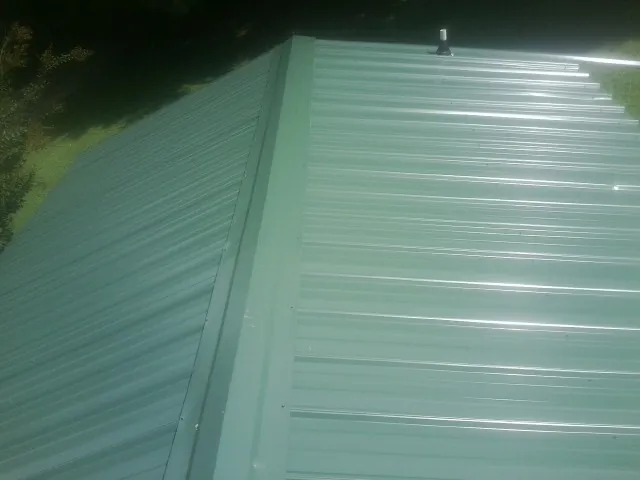 New green metal panels meeting at the ridge of a roof — Flat Roof Repair work by our crew in Rio Medina