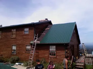 Green metal roof going on a two story log home with ladders set in Rio Medina