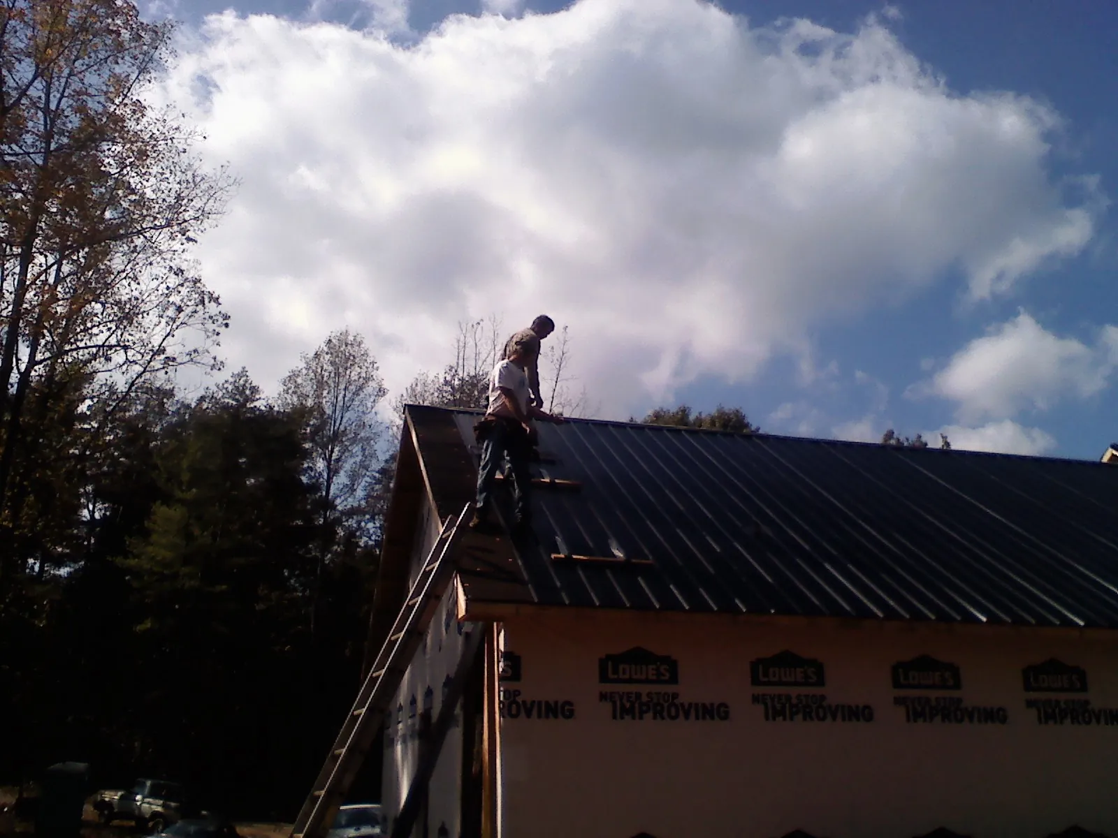 Roofer fastening dark metal panels high against a cloudy sky, from a Roof Inspection job in Rio Medina
