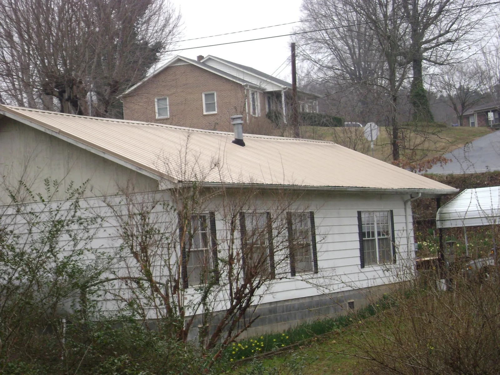 Tan metal roof on a white sided house set into a hillside — Commercial Roofing by Roofing Brothers in Rio Medina